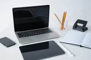 laptop na białym biurku obok notes