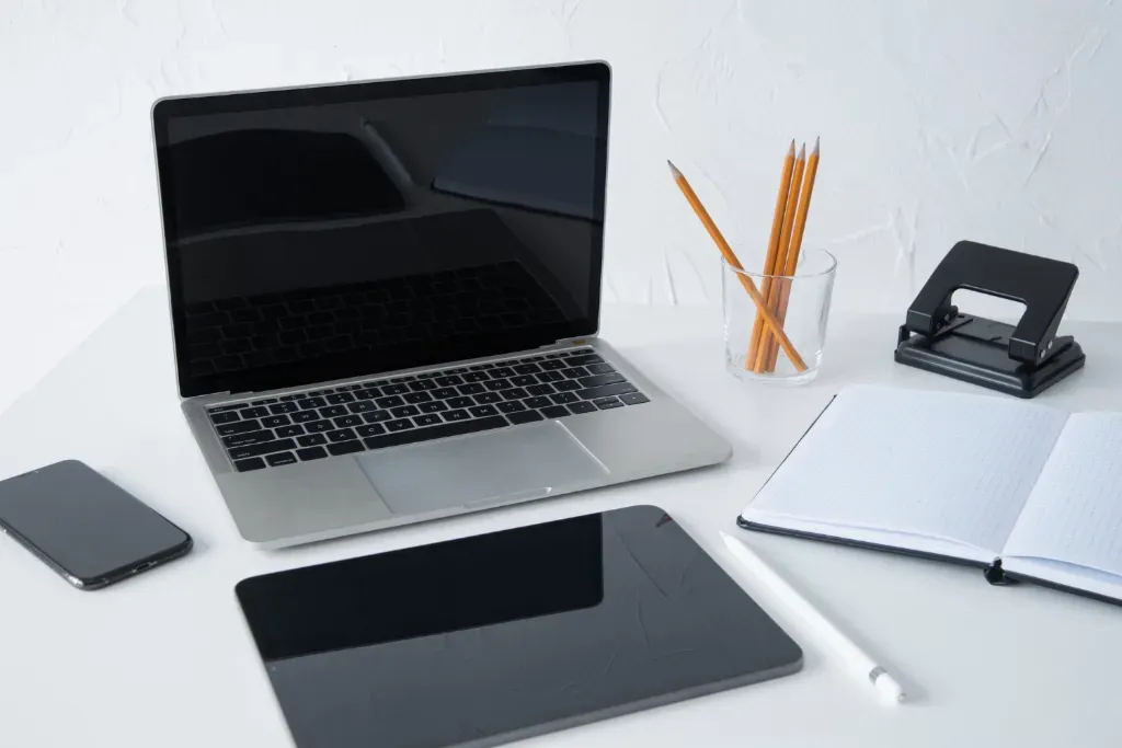 laptop na białym biurku obok notes